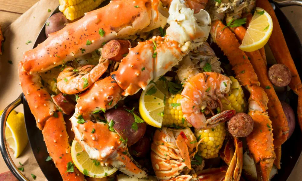 Top view of Cajun seafood boil platter with king crab legs, shrimp, corn, potatoes, sausage, lemon wedges and parsley garnish.